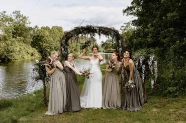 Bride and bridesmaids at outdoor floral arch by river